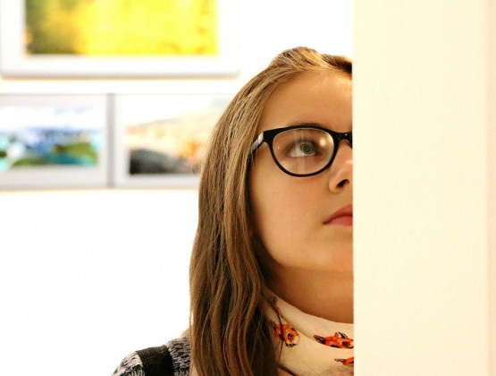 Eine junge Frau mit Brille steht vor einem Bild