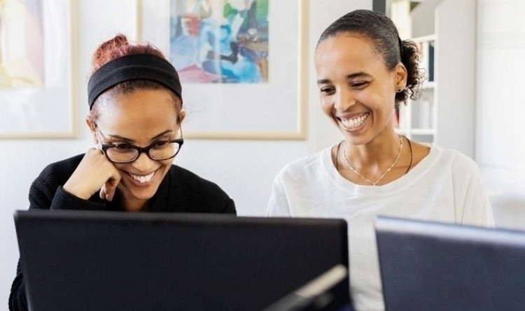 Zwei Frauen lächelnd vor einem Laptop